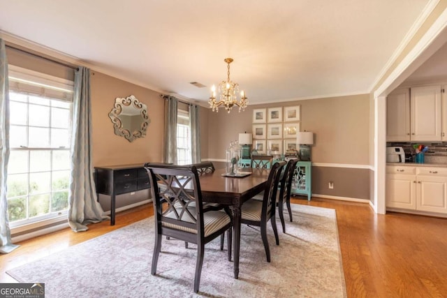 dining space with light hardwood / wood-style floors, crown molding, plenty of natural light, and a notable chandelier