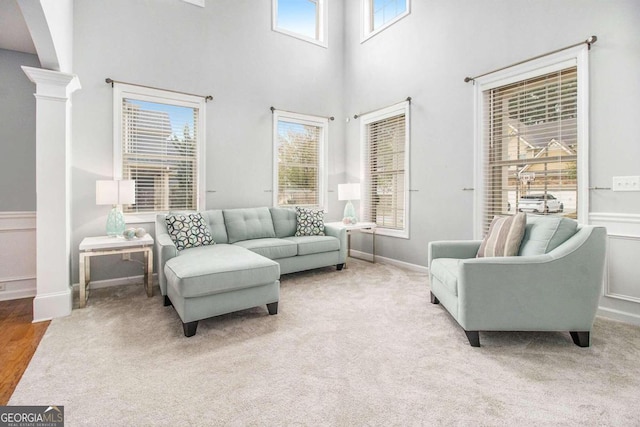 living room featuring light carpet, a towering ceiling, ornate columns, and a healthy amount of sunlight