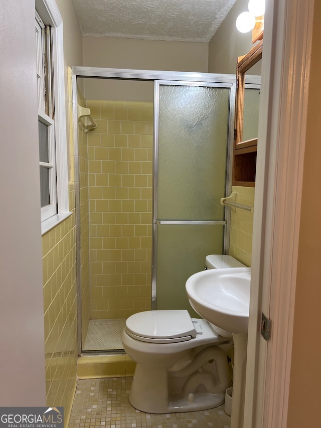 bathroom featuring a textured ceiling, toilet, a shower with door, and tile patterned flooring