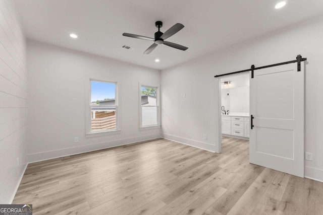 unfurnished bedroom with light hardwood / wood-style floors, connected bathroom, ceiling fan, and a barn door