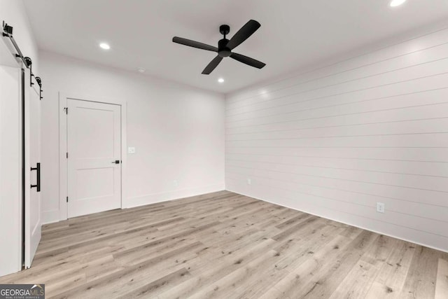 empty room with light hardwood / wood-style floors, ceiling fan, and a barn door