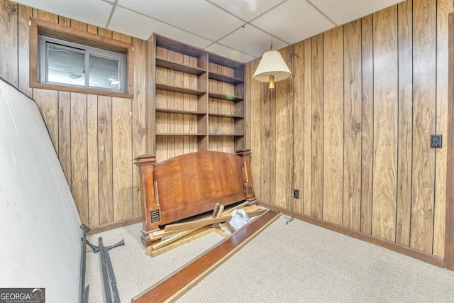 interior space with a paneled ceiling, carpet flooring, and wooden walls