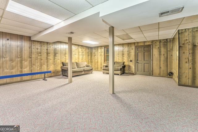 basement with carpet flooring, a drop ceiling, and wooden walls