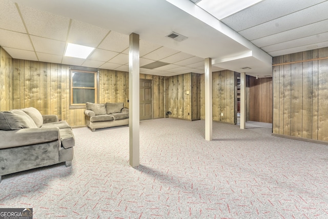 basement with carpet, a drop ceiling, and wooden walls