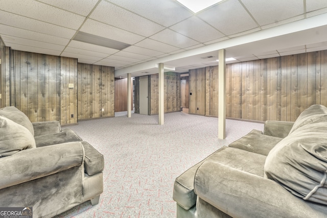 basement featuring a drop ceiling, carpet floors, and wooden walls