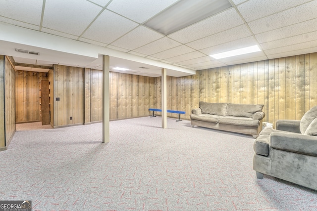 basement with carpet, a paneled ceiling, and wood walls