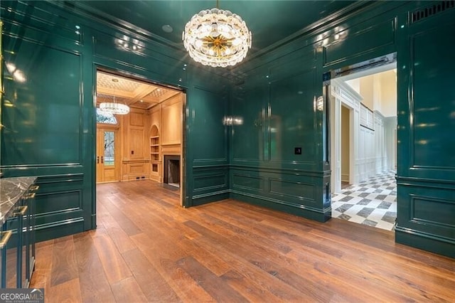 spare room with crown molding, wood finished floors, a decorative wall, a chandelier, and arched walkways