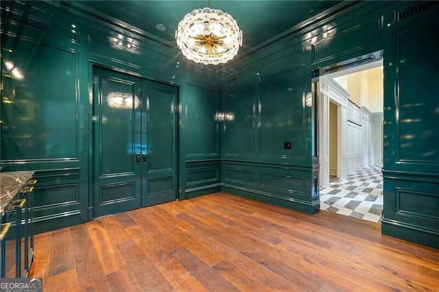 spare room with ornamental molding, a chandelier, wood finished floors, and a decorative wall