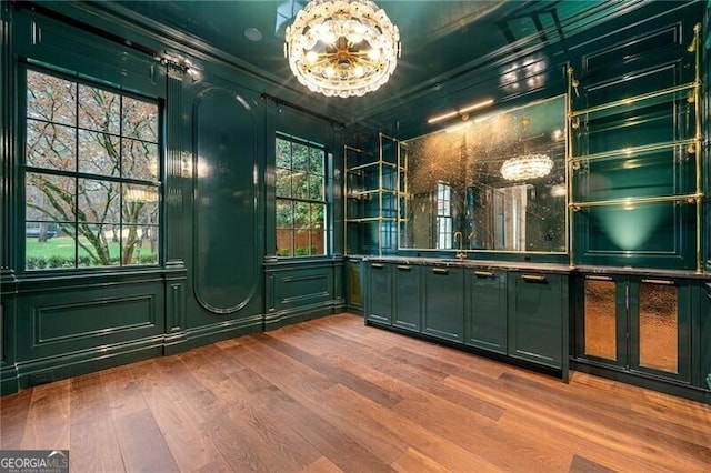 bar featuring ornamental molding, a sink, a notable chandelier, wood finished floors, and a decorative wall