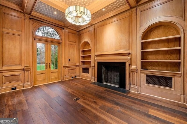 unfurnished living room with ornamental molding, dark wood finished floors, built in features, a fireplace, and french doors