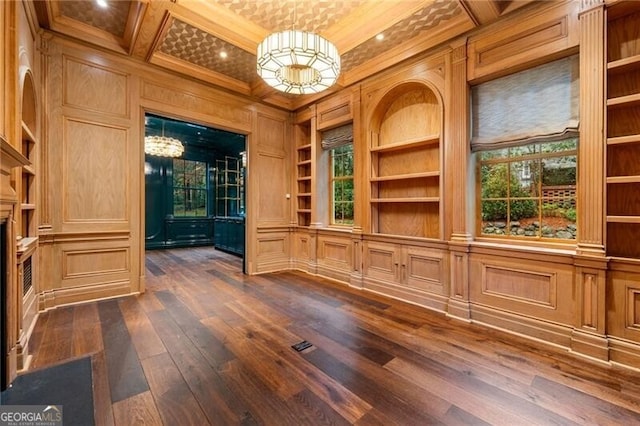 interior space featuring ornamental molding, coffered ceiling, a fireplace with flush hearth, dark wood finished floors, and built in shelves