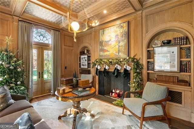 living area featuring ornamental molding, built in shelves, coffered ceiling, a decorative wall, and a warm lit fireplace