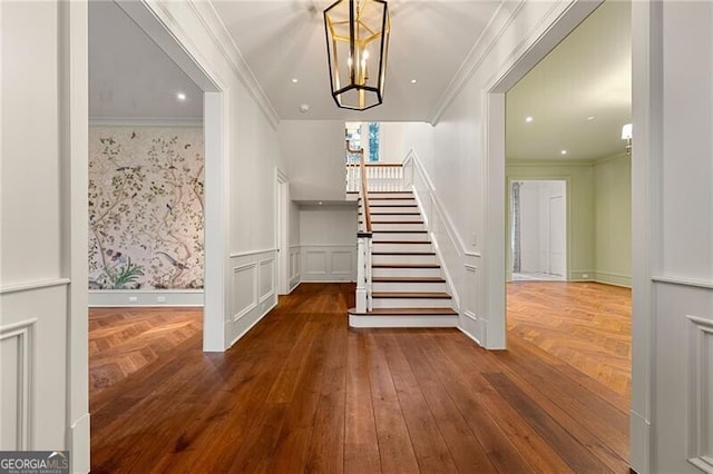 stairs with ornamental molding, parquet floors, a notable chandelier, wainscoting, and a decorative wall