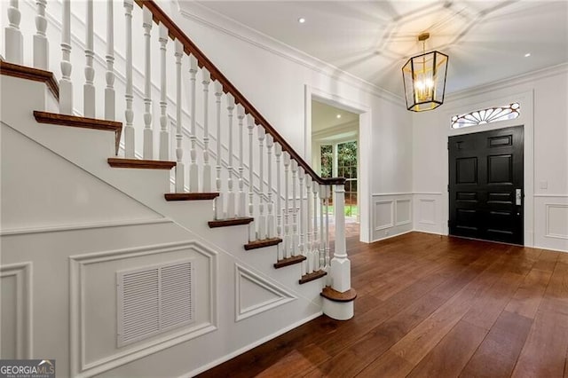 entrance foyer featuring a decorative wall, ornamental molding, visible vents, and dark wood-type flooring