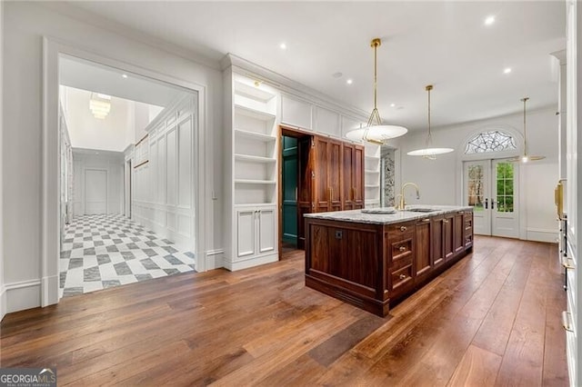 kitchen featuring a sink, dark wood-type flooring, a kitchen island with sink, a decorative wall, and french doors