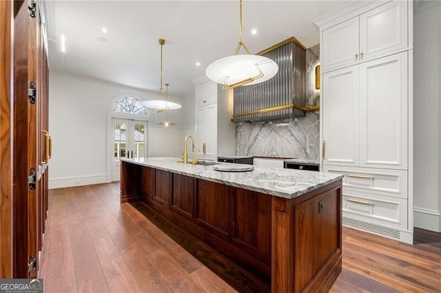 kitchen with a kitchen island with sink, light stone counters, white cabinets, and hanging light fixtures