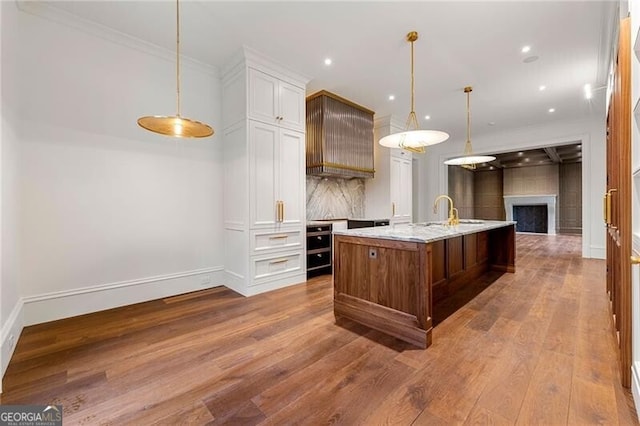 kitchen with wood finished floors, a large island, light stone countertops, decorative light fixtures, and white cabinetry