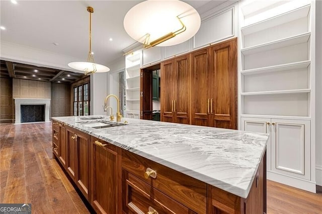 kitchen featuring a sink, a center island with sink, light wood finished floors, brown cabinetry, and a fireplace