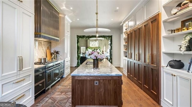 kitchen featuring light stone counters, a center island with sink, pendant lighting, and open shelves