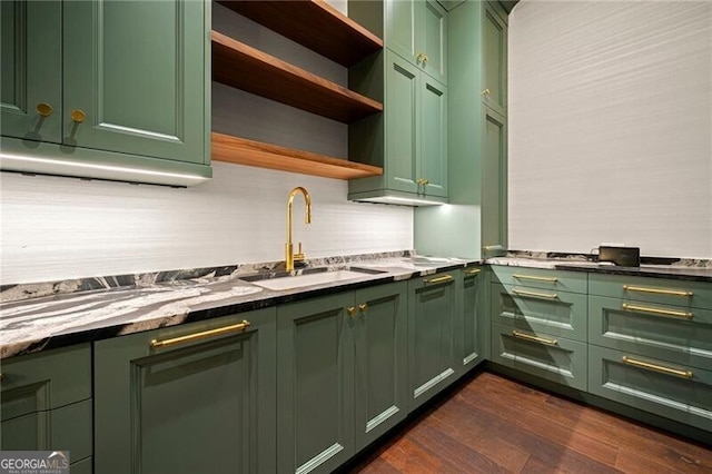 kitchen featuring decorative backsplash, a sink, dark wood finished floors, light stone countertops, and green cabinets