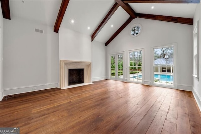 unfurnished living room featuring visible vents, high vaulted ceiling, beam ceiling, a fireplace with flush hearth, and wood finished floors