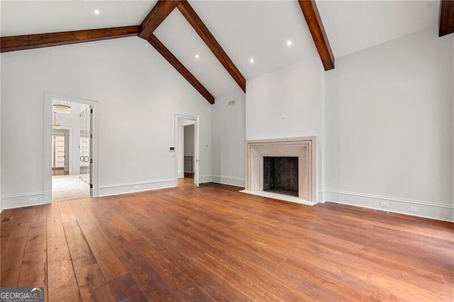 unfurnished living room with light wood finished floors, baseboards, high vaulted ceiling, a fireplace with flush hearth, and beamed ceiling