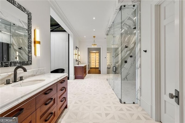 full bath featuring crown molding, a marble finish shower, a sink, and two vanities