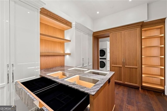 kitchen featuring dark wood finished floors, brown cabinets, stacked washer and dryer, and open shelves