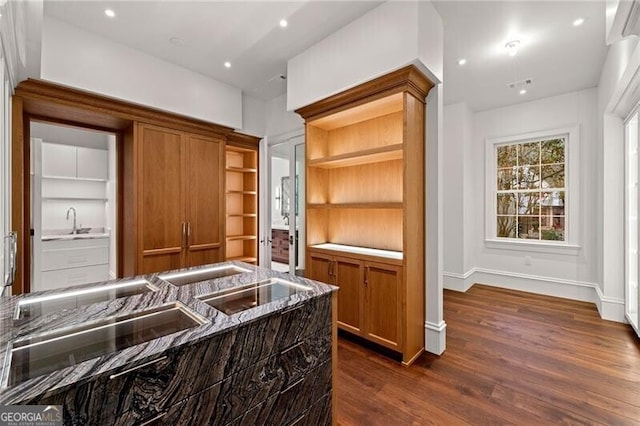 kitchen featuring a sink, recessed lighting, dark stone counters, brown cabinets, and dark wood finished floors