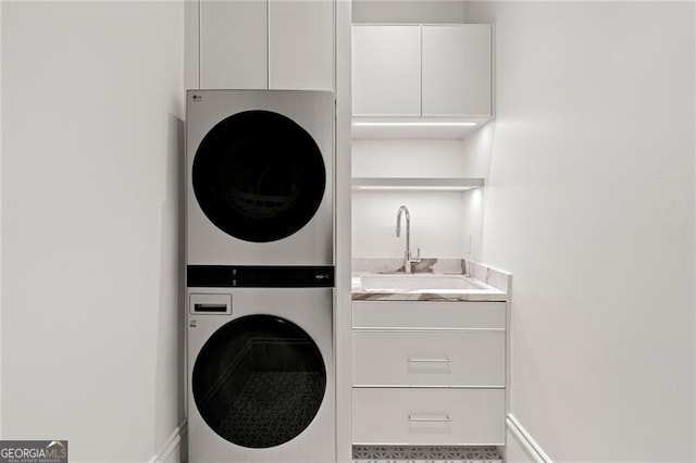 clothes washing area featuring stacked washer / drying machine, baseboards, cabinet space, and a sink