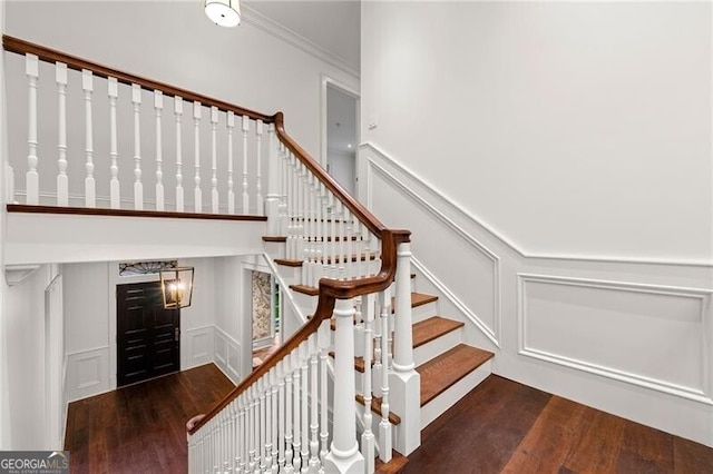 stairway with ornamental molding, wood finished floors, and a decorative wall