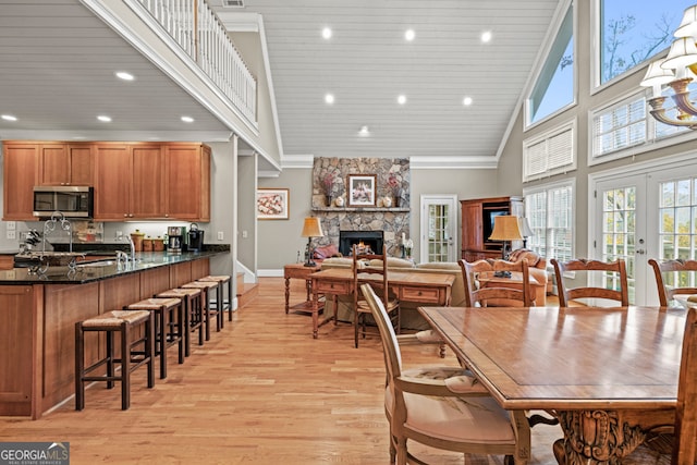 dining area featuring a fireplace, high vaulted ceiling, light hardwood / wood-style floors, and ceiling fan with notable chandelier