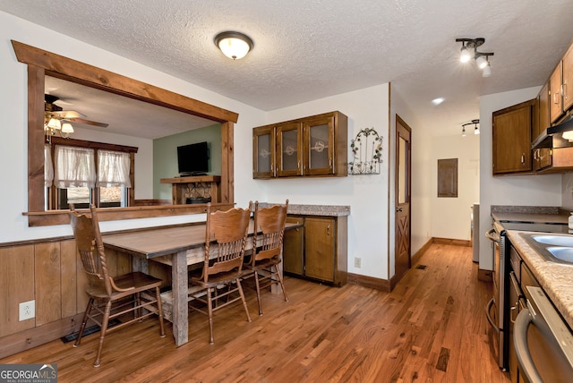 dining area with ceiling fan, wooden walls, wood-type flooring, and a textured ceiling