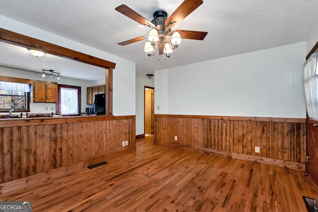 unfurnished living room featuring a textured ceiling, hardwood / wood-style flooring, ceiling fan, and wooden walls