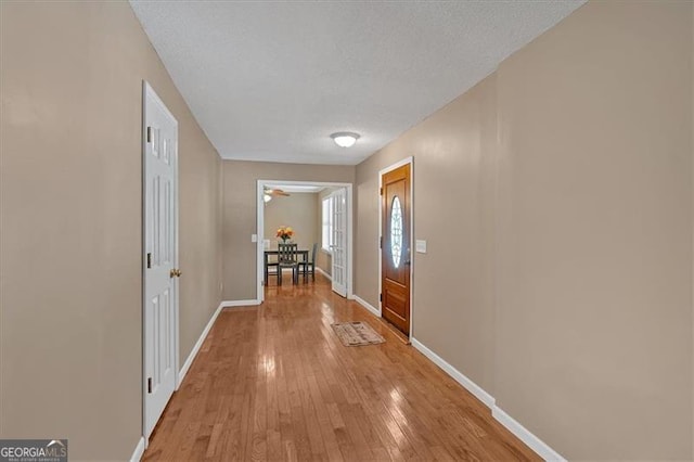 corridor with a textured ceiling and light wood-type flooring