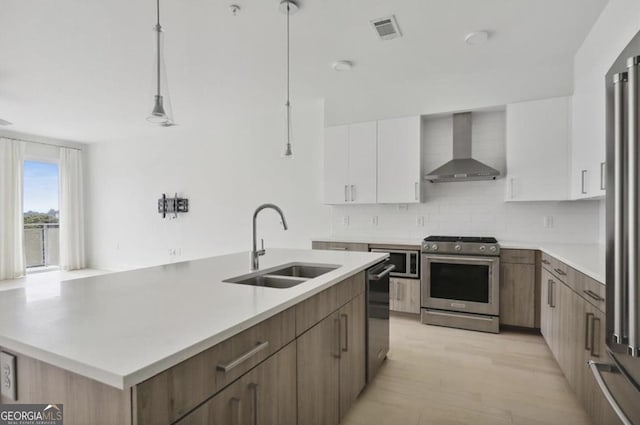 kitchen featuring appliances with stainless steel finishes, decorative light fixtures, white cabinetry, sink, and wall chimney exhaust hood