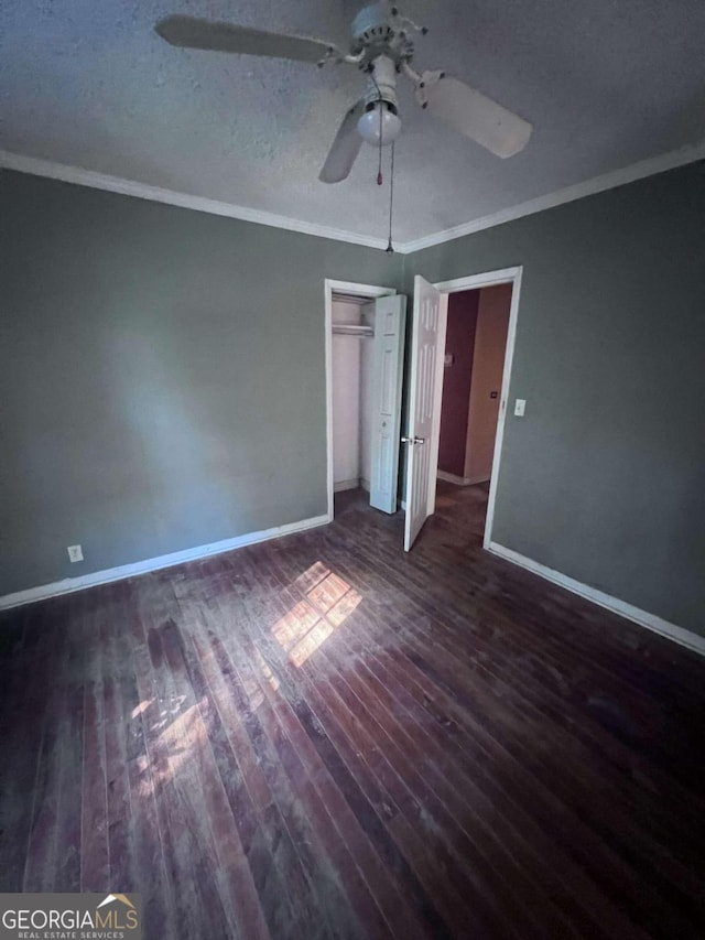 unfurnished bedroom featuring crown molding, ceiling fan, a closet, and dark wood-type flooring