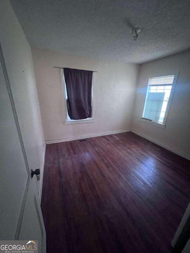 spare room featuring a textured ceiling and dark hardwood / wood-style floors