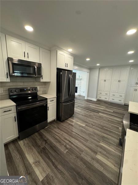 kitchen with tasteful backsplash, white cabinetry, dark wood-type flooring, and appliances with stainless steel finishes