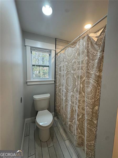 bathroom with wood-type flooring, toilet, and a shower with curtain