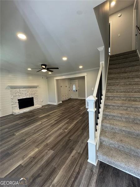 unfurnished living room featuring dark hardwood / wood-style floors, a stone fireplace, ceiling fan, and crown molding