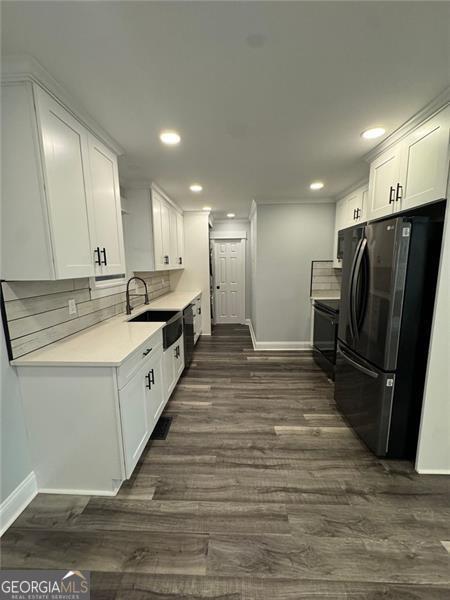 kitchen with black refrigerator, tasteful backsplash, dark wood-type flooring, sink, and white cabinetry