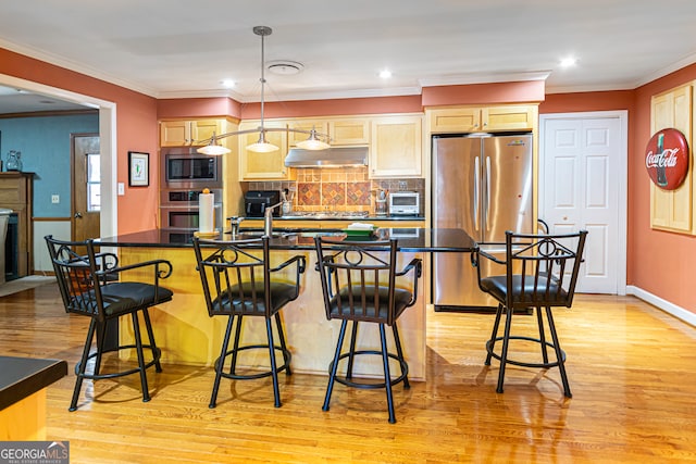 kitchen with appliances with stainless steel finishes, light brown cabinets, a center island with sink, light hardwood / wood-style flooring, and a breakfast bar area