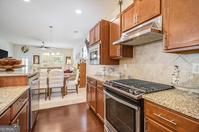 kitchen with light stone countertops, ceiling fan with notable chandelier, stainless steel appliances, decorative light fixtures, and dark hardwood / wood-style floors