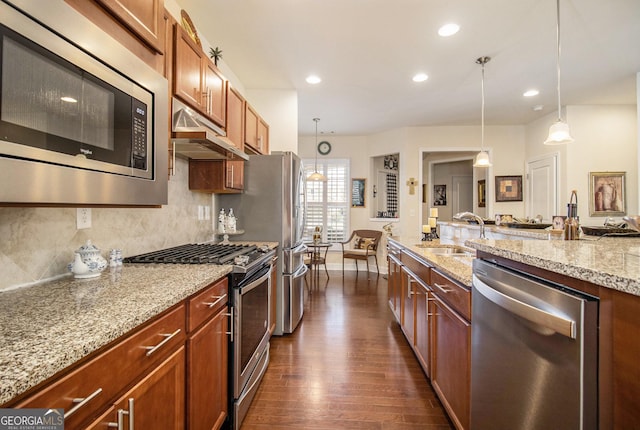 kitchen with backsplash, sink, appliances with stainless steel finishes, decorative light fixtures, and light stone counters