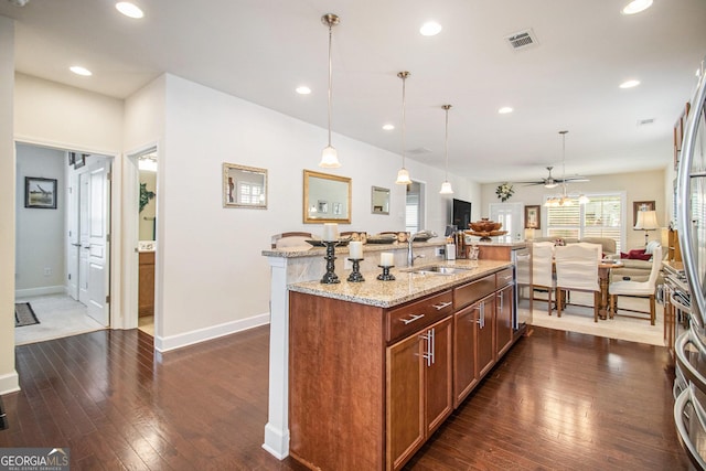 kitchen with pendant lighting, a kitchen island with sink, sink, ceiling fan, and light stone counters