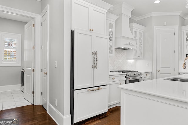 kitchen featuring high end appliances, premium range hood, dark wood-type flooring, sink, and white cabinetry