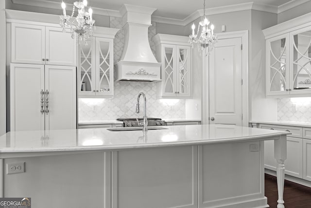 kitchen featuring white cabinets, decorative light fixtures, premium range hood, and an island with sink