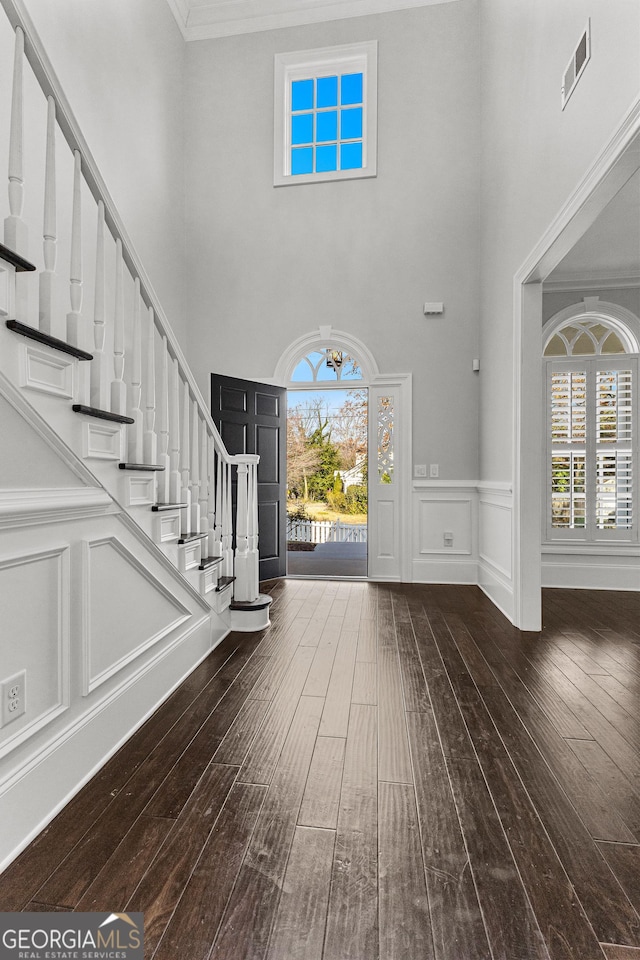 entryway with a towering ceiling, dark hardwood / wood-style floors, and ornamental molding