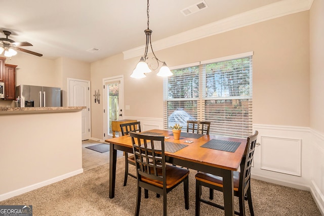 dining area with light colored carpet, ceiling fan with notable chandelier, and ornamental molding